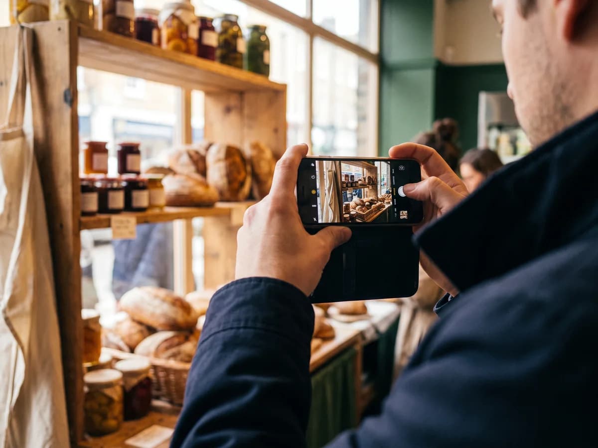 Hände filmen mit dem Handy eine Auslage mit Brot und Eingemachtem